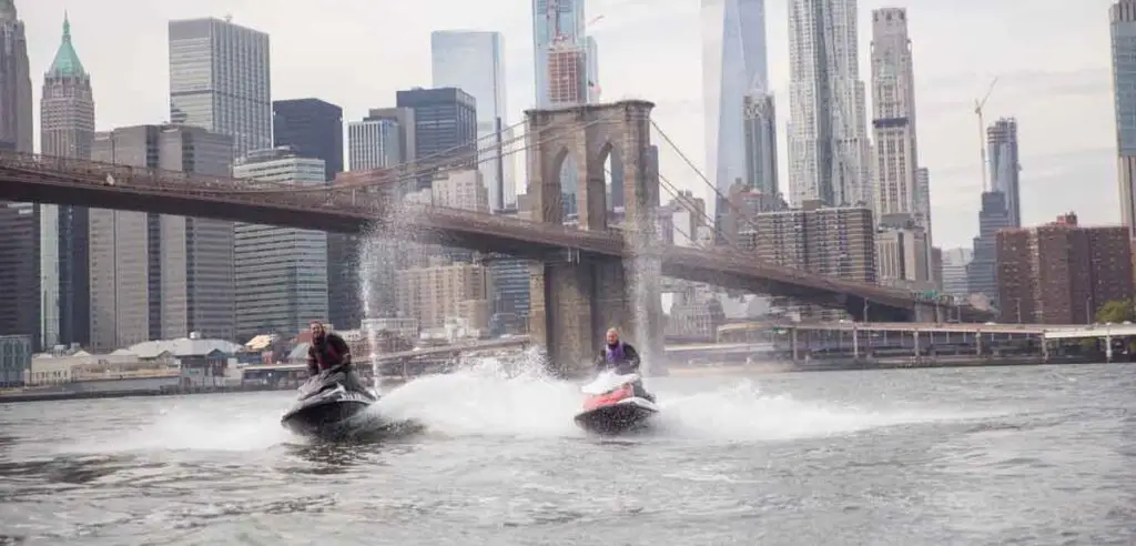 a man riding a boat on the water with a city in the background