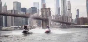 a man riding a boat on the water with a city in the background