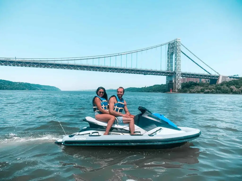 Couple riding a jet ski together on the Hudson River in front of a bridge