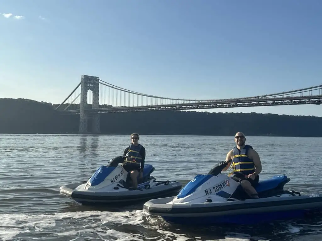 Couple riding jet skis side by side on the Hudson River in front of a bridge