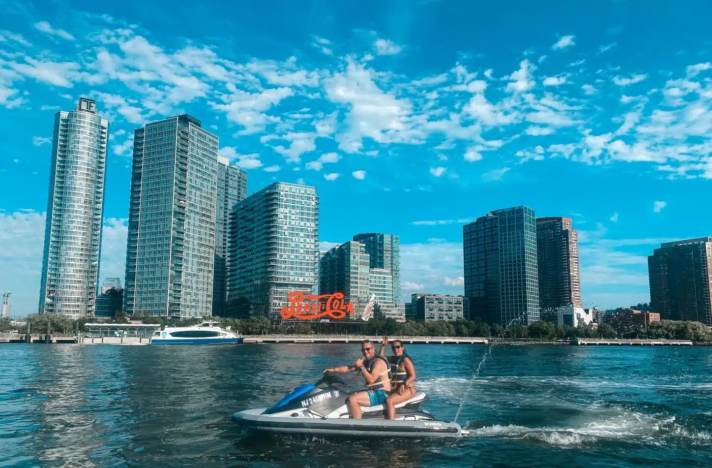 Riders on a jet ski in New York Harbor with waterfront skyscrapers behind them