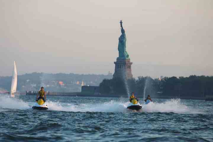 people jet skiing in front of the statue of liberty