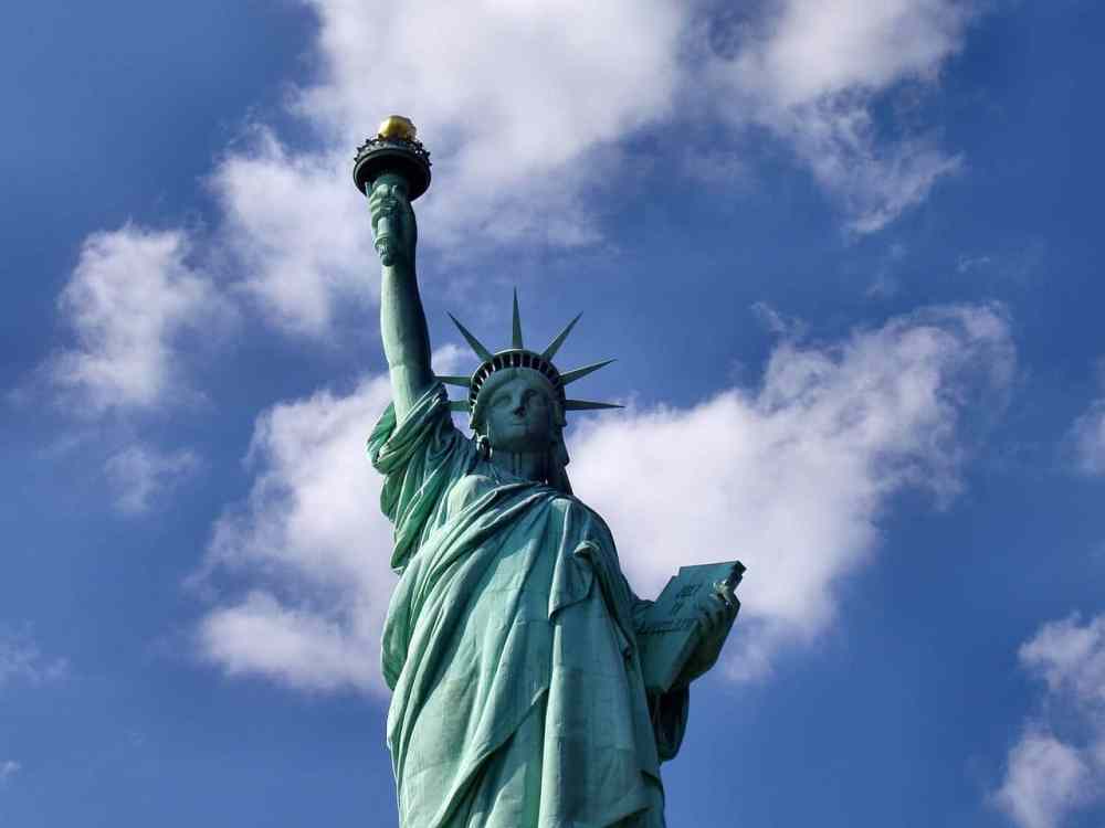 a green statue on a cloudy day with Statue of Liberty in the background