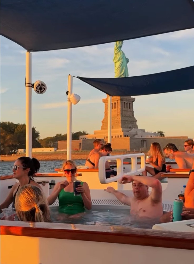People in a boat hot tub with Statue of Liberty in the background at sunset.