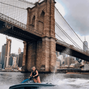 a person riding on the back of a boat next to Brooklyn Bridge