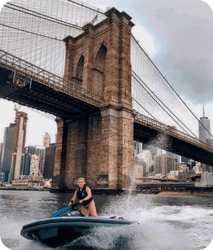 a person riding on the back of a boat next to Brooklyn Bridge